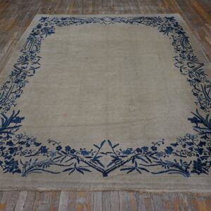 Pale gray rug with a vibrant blue botanical border covers distressed hardwood flooring.
