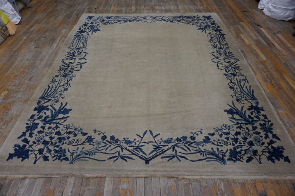 Pale gray rug with a vibrant blue botanical border covers distressed hardwood flooring.