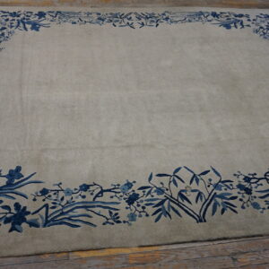 Light gray low pile rug with a wide blue botanical border sits on distressed wood flooring.