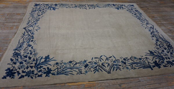 Light gray low pile rug with a wide blue botanical border sits on distressed wood flooring.