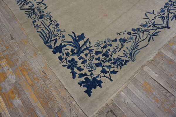 Greige rug corner with a dense indigo floral border resting on worn wooden planks.