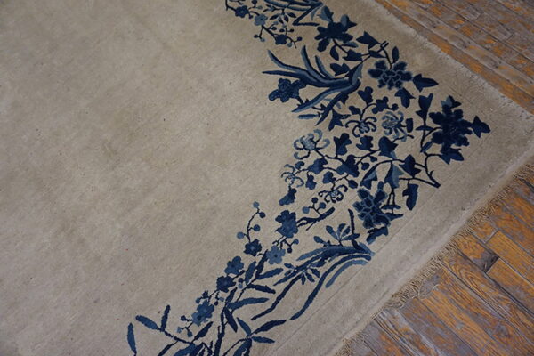 Low pile beige rug featuring a detailed blue floral border rests on distressed hardwood floors.