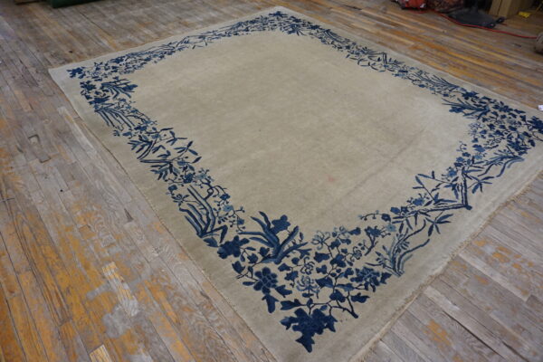 Pale beige rug featuring a detailed dark blue botanical border resting on weathered wooden planks.