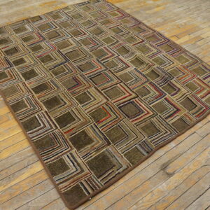 Textured olive and multicolored geometric patterned rug lying on distressed light hardwood flooring.