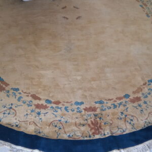 Round tan rug with a wide navy border and a decorative band of blue and terracotta florals on tile.