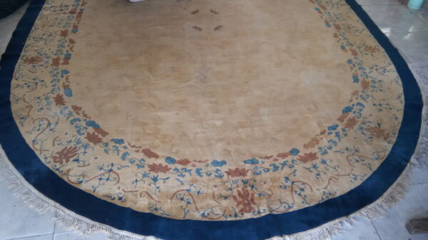 Round tan rug with a wide navy border and a decorative band of blue and terracotta florals on tile.