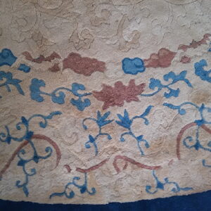 Detail of a textured beige rug with blue and reddish-brown floral patterns and a navy edge.