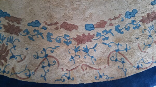 Detail of a textured beige rug with blue and reddish-brown floral patterns and a navy edge.