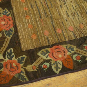 Dark brown and coral floral hooked rug border next to a textured tan field, visible on light wood planks.