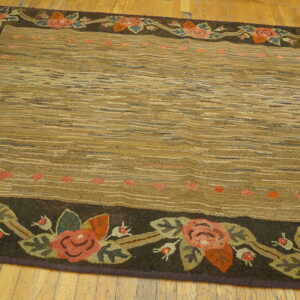 Brown textured rug with a striated field and a dark floral border featuring red roses on wood flooring.