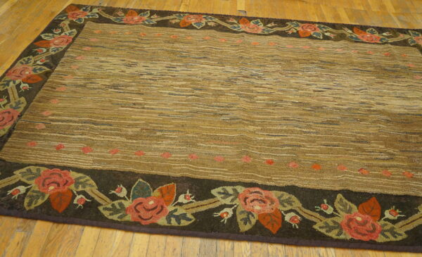 Brown textured rug with a striated field and a dark floral border featuring red roses on wood flooring.