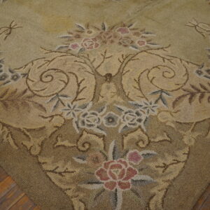 Muted tan and green rug with dense texture and rose floral pattern lies on worn wooden planks.
