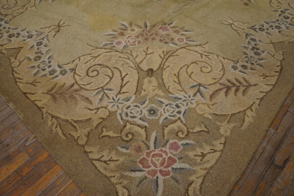 Muted tan and green rug with dense texture and rose floral pattern lies on worn wooden planks.