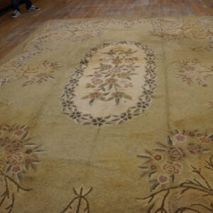 A large, pale green and beige botanical rug with a central medallion rests on a wood floor.