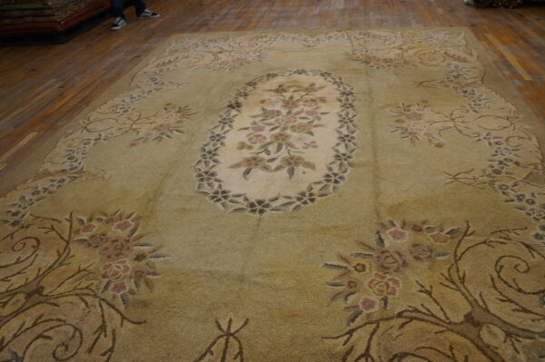 A large, pale green and beige botanical rug with a central medallion rests on a wood floor.