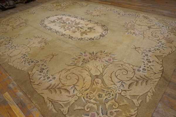Large green and tan rug with intricate floral designs and a thick texture lying on distressed wood planks.
