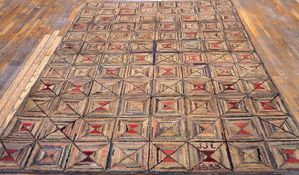 Textured rug featuring beige and brown geometric quilt-like squares with red accents displayed on hardwood flooring.