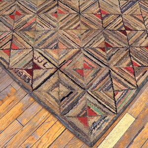 Rustic hooked rug corner with geometric brown and red patterns rests on distressed wood flooring.