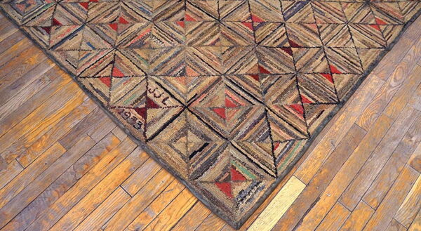 Rustic hooked rug corner with geometric brown and red patterns rests on distressed wood flooring.