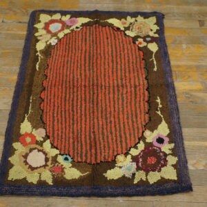 Looped rug with red and green stripes, colorful floral motifs, and a dark brown border on worn wood flooring.