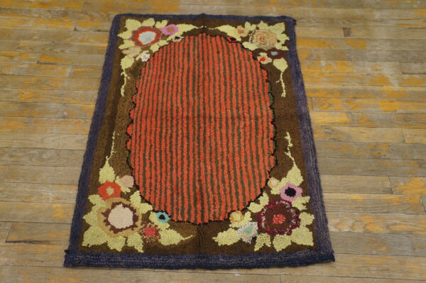 Looped rug with red and green stripes, colorful floral motifs, and a dark brown border on worn wood flooring.