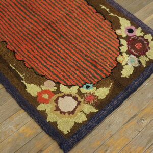 High-pile rug with orange and green stripes, detailed multicolored floral border, and navy edge on wood flooring.
