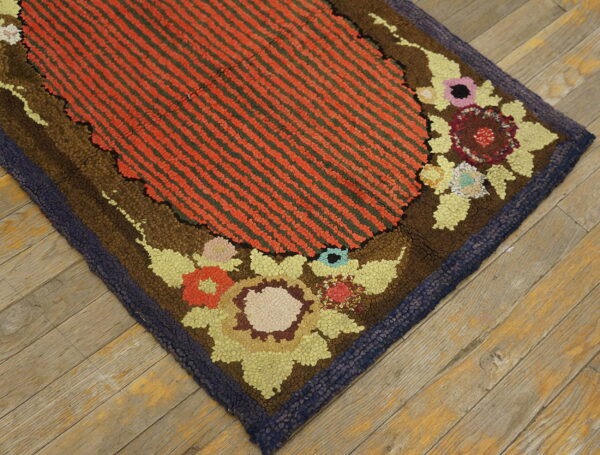 High-pile rug with orange and green stripes, detailed multicolored floral border, and navy edge on wood flooring.