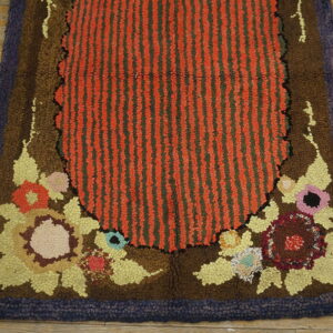 Chunky hooked rug with a striped red center, brown floral details, and a dark purple perimeter border.