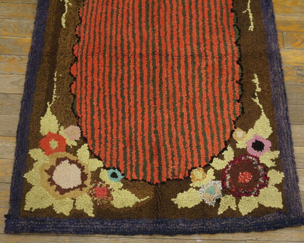 Chunky hooked rug with a striped red center, brown floral details, and a dark purple perimeter border.