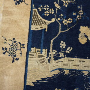 Navy blue rug detail featuring a tan chinoiserie pavilion and floral design next to wood flooring.