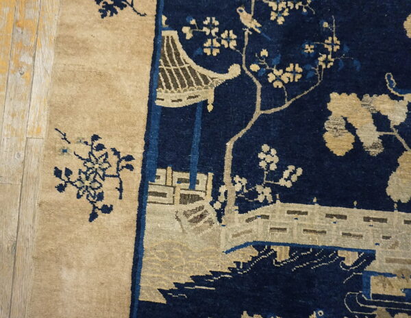 Navy blue rug detail featuring a tan chinoiserie pavilion and floral design next to wood flooring.