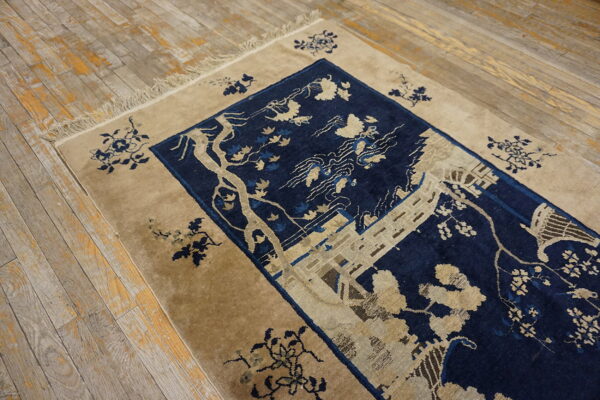 Deep blue rug featuring a detailed tan botanical pattern, bordered with fringe on rustic hardwood floors.