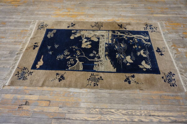 Navy field rug with a detailed tan scenic pattern and floral border on rustic wooden floorboards.