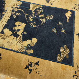 Detailed low pile rug in deep blue and tan featuring a central scene of buildings, trees, and flying birds.