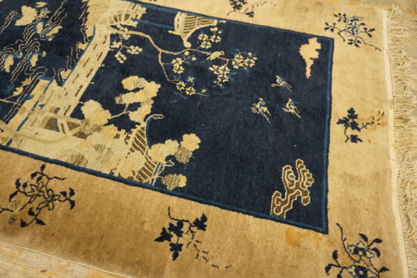 Detailed low pile rug in deep blue and tan featuring a central scene of buildings, trees, and flying birds.