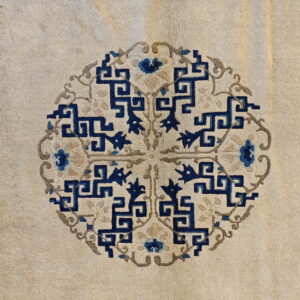 Beige rug surface showing a circular medallion with angular dark blue and subtle gray floral motifs.