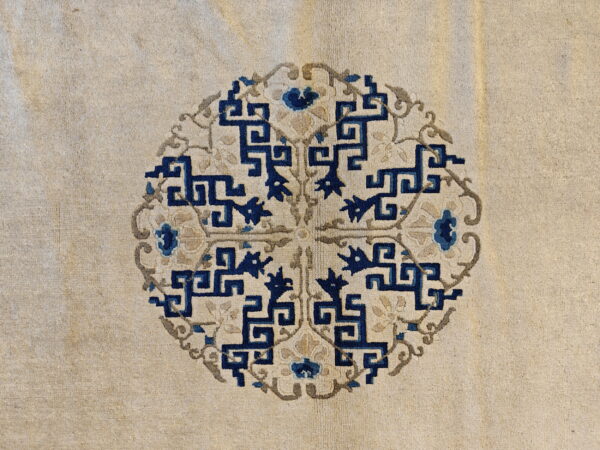Beige rug surface showing a circular medallion with angular dark blue and subtle gray floral motifs.