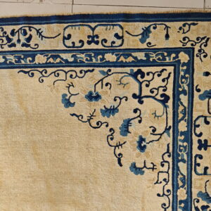 Beige rug with deep blue floral corner pattern and multiple decorative borders on tile flooring.