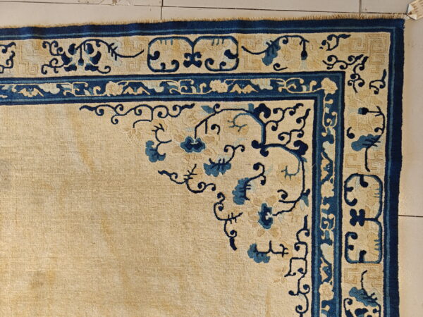 Beige rug with deep blue floral corner pattern and multiple decorative borders on tile flooring.