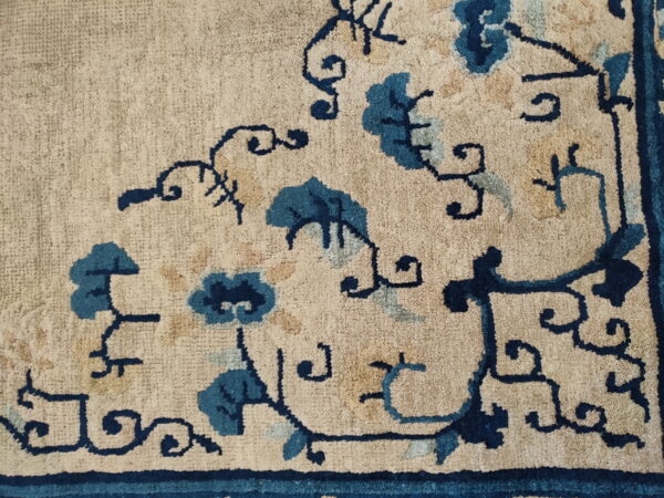 Beige rug corner with detailed floral scrolling design in deep indigo and lighter teal blue.