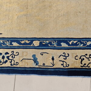 Beige rug with a detailed navy and light blue foliate border resting on light tiled flooring.