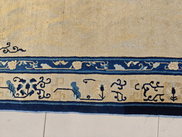 Beige rug with a detailed navy and light blue foliate border resting on light tiled flooring.