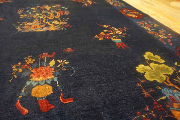 Close-up of a navy rug with plush pile and colorful botanical motifs resting on light wood flooring.