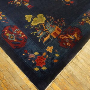 A dark blue rug corner featuring red, gold, and green scenic motifs rests on light wood plank flooring.