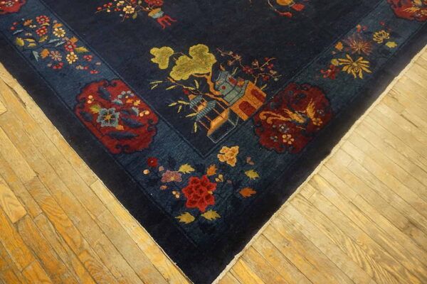 A dark blue rug corner featuring red, gold, and green scenic motifs rests on light wood plank flooring.