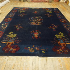 A large dark blue rug featuring multicolored pictorial and floral patterns rests on distressed blonde wood flooring.