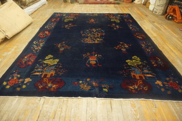 A large dark blue rug featuring multicolored pictorial and floral patterns rests on distressed blonde wood flooring.