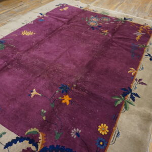 Shimmering purple rug with multicolored floral design and taupe border on rustic wood planks.
