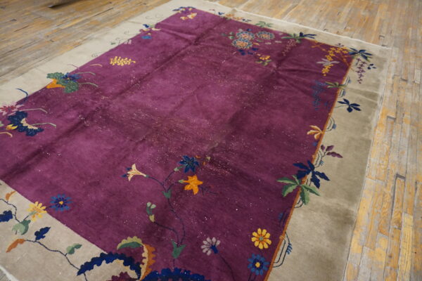 Shimmering purple rug with multicolored floral design and taupe border on rustic wood planks.