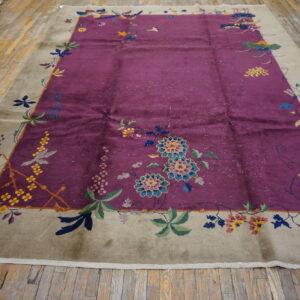 Lustrous magenta rug with a colorful floral pattern and wide taupe border rests on worn hardwood planks.